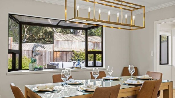 Un coin repas avec une table en verre, des chaises marron et un lustre.