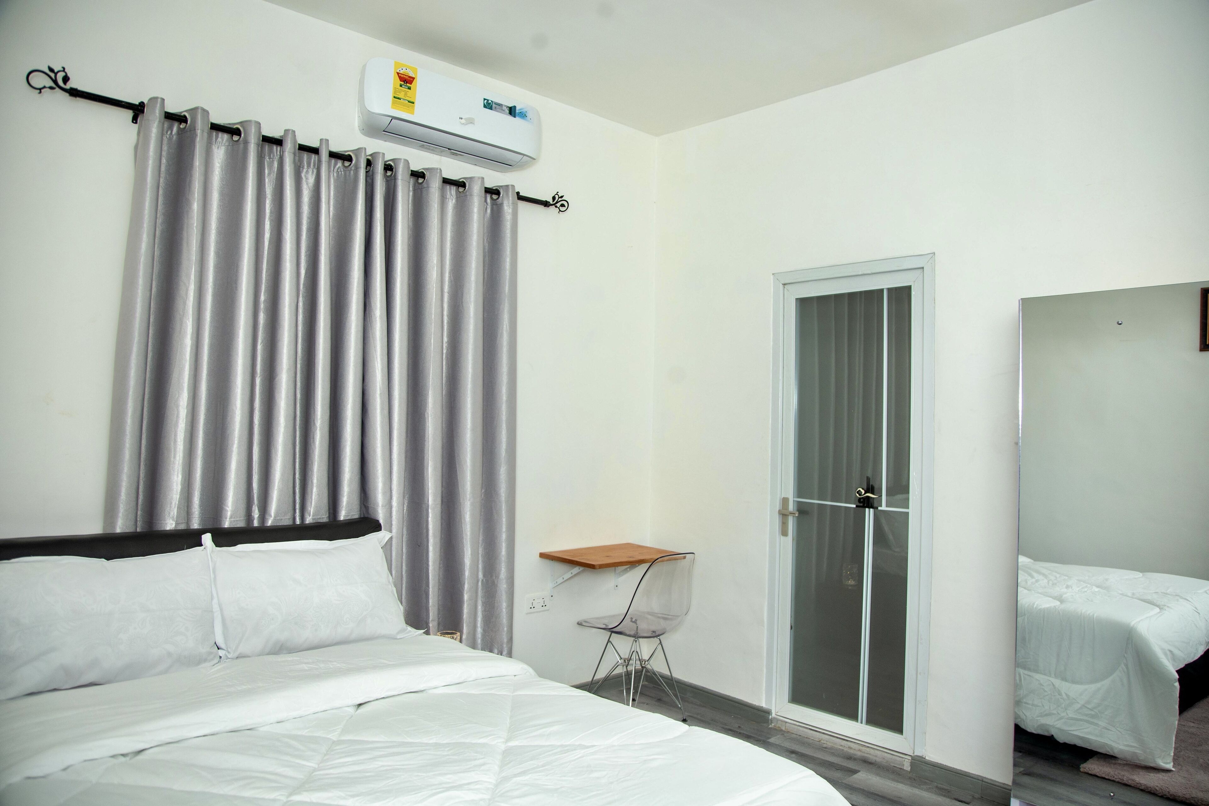Una habitación de hotel con una cama, una silla, una mesita pequeña, un ventanal corredero y un equipo de aire acondicionado.