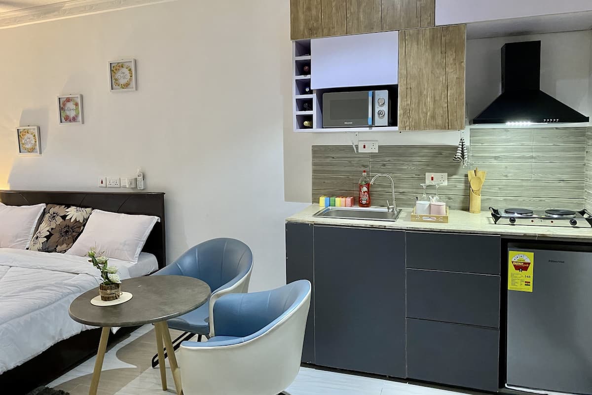 Una habitación de hotel compacta con cama, mesita de noche y una pequeña kitchenette.