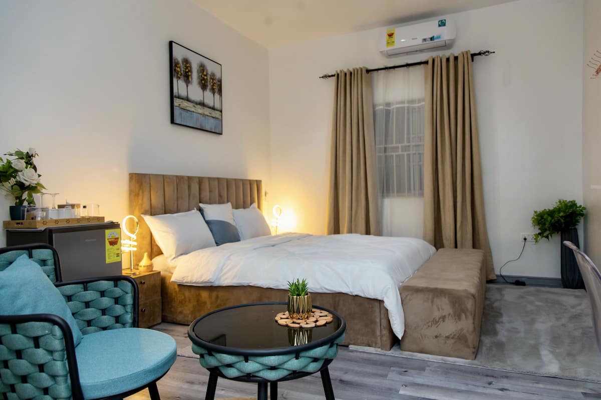 Una habitación de hotel con cama, mesita de noche, lámpara y una pequeña mesa redonda con una planta.