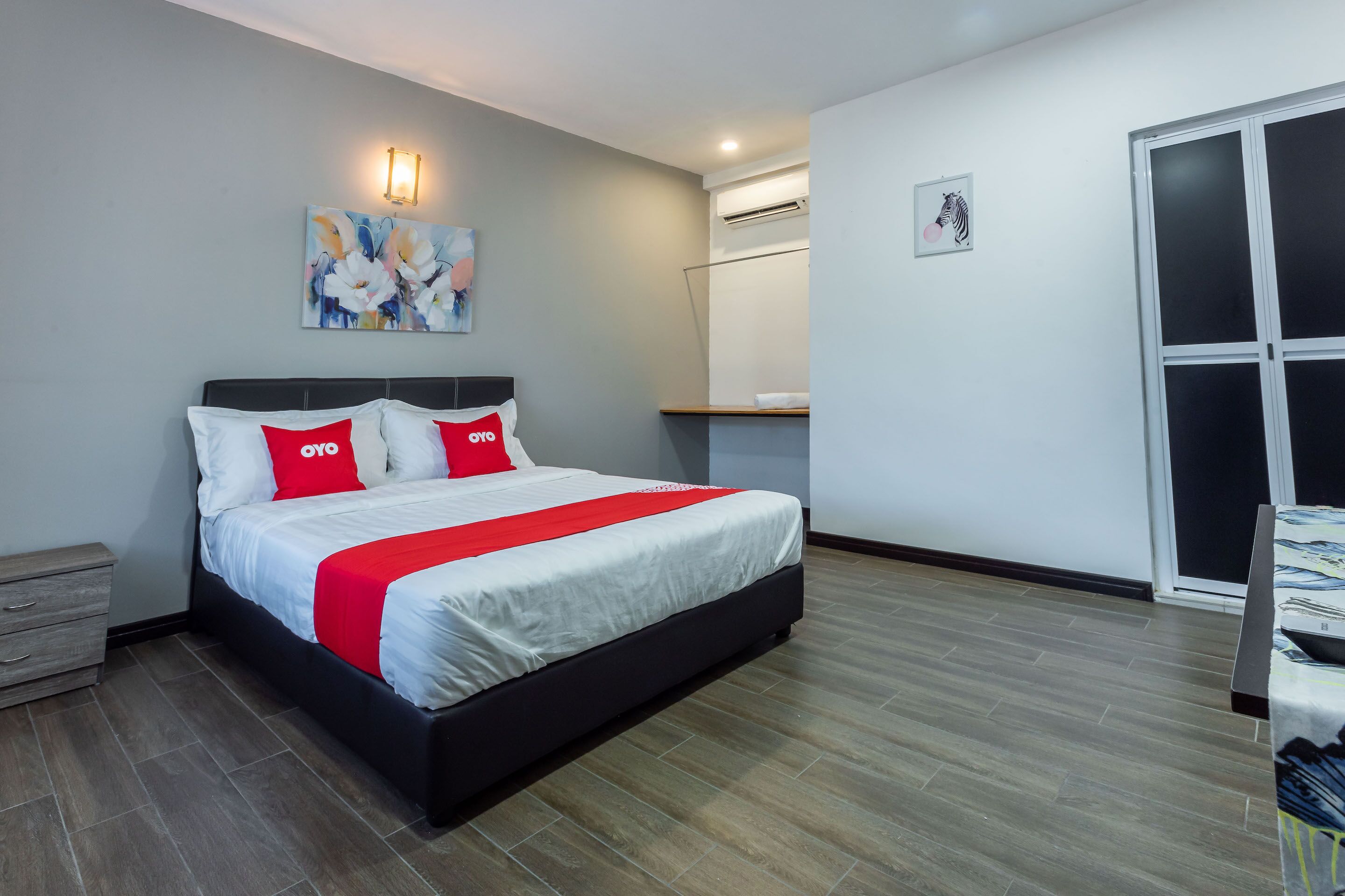 Une chambre moderne avec un grand lit, une table de chevet, une œuvre d’art accrochée au mur, un appareil de climatisation et une porte coulissante.