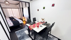 A compact room with a bed, a dining table, and chairs. There is a small table with a vase and a candle. The room has a simple, modern design with a black and white color scheme. - Full Renovation/tamade Station 4 Min/2ldk/max 8 Persons (Osaka)