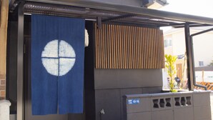 A residential building with a dark exterior, a tiled entrance, and a blue curtain with a white design. - Full Renovation/tamade Station 4 Min/2ldk/max 8 Persons (Osaka)