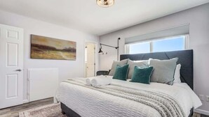 A modern bedroom with a large bed, a painting on the wall, and a window with blinds. - Panoramic Point - Downtown King Full Kitchen (Colorado Springs)