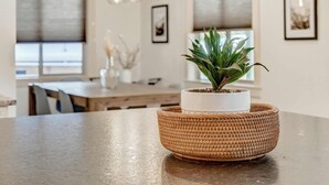 Et moderne køkken med spisebord, hængende pendellamper og en stueplante i en vævet kurv.