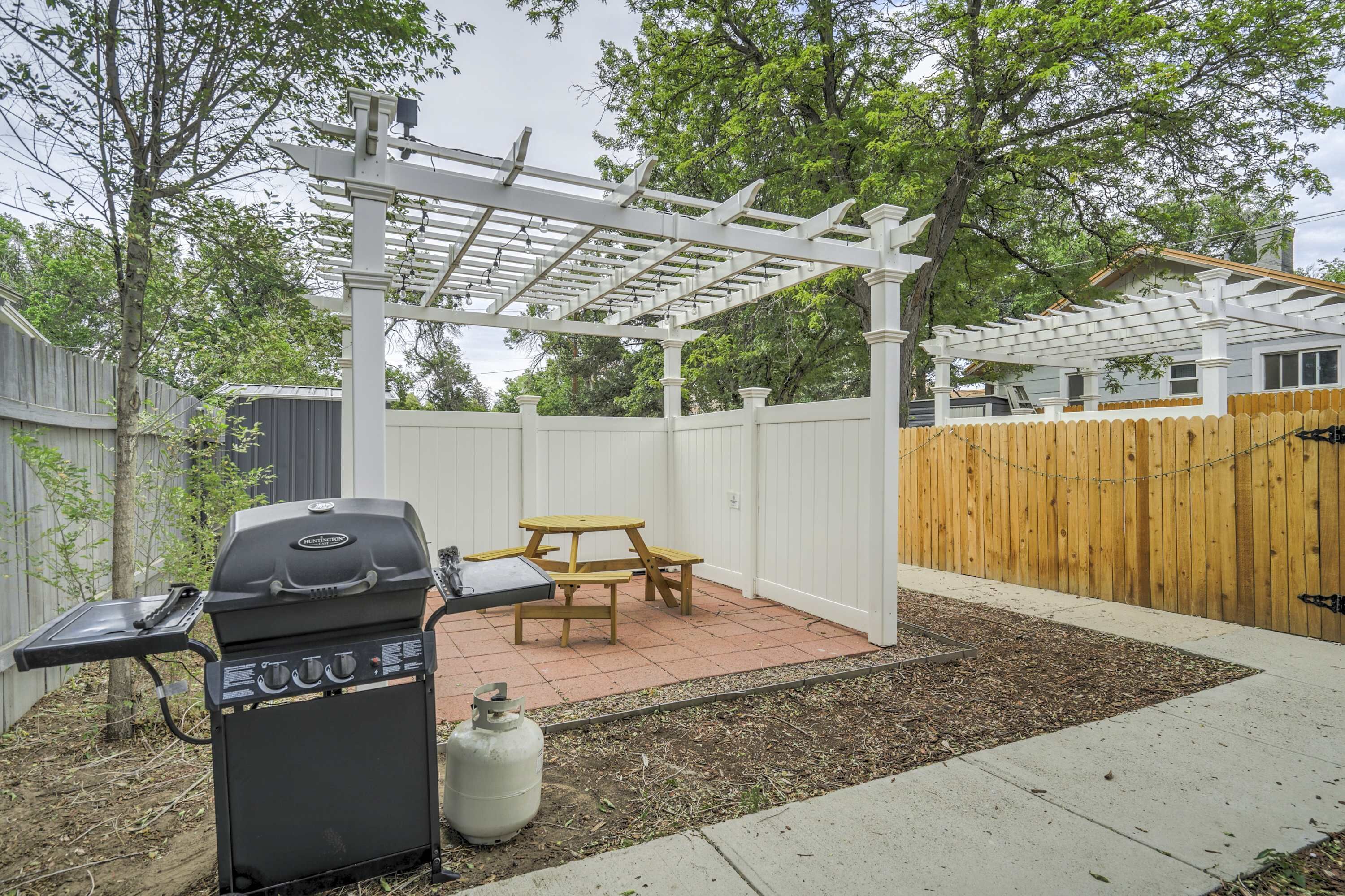 Un jardin avec un barbecue, une table de pique-nique, une pergola et une clôture en bois.
