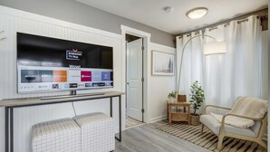 Een moderne woonkamer met een wandgemonteerde televisie waarop diverse streaming apps getoond worden, een bank, een stoel, een kleine tafel met een plant, en een deur die naar een andere kamer leidt.