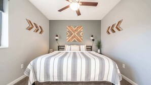 Une chambre à coucher avec un lit, un ventilateur de plafond et des œuvres d’art décoratives au mur.