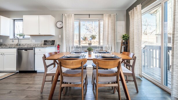Une cuisine moderne avec des meubles blancs, un lave-vaisselle en acier inoxydable et un coin repas comprenant une table et des chaises en bois.