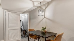 En hyggelig spiseplads med et bord, stole, en hængende lampe og udsigt til et vaskerum.