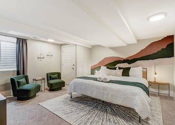 Welcome to Institute Den! Unwind in the plush comfort of this serene bedroom, featuring a cozy queen bed and vibrant mountain mural, perfect for your Colorado Springs adventure