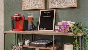 En kaffestation med en Keurig-maskine, en kopholder og et skilt med teksten "VELKOMMEN TIL COLORADO #RENJOY".