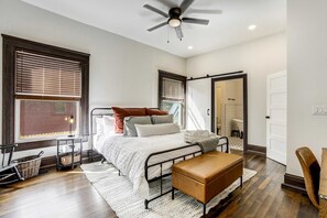 Un dormitorio con cama, mesitas de noche, un banco, ventilador de techo y vistas al exterior.