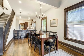 Un comedor amplio con una mesa y sillas de madera, una cocina al fondo y una escalera que sube a un nivel superior.