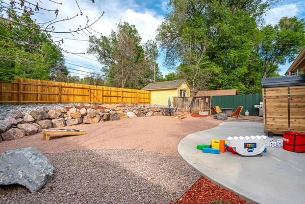 Un patio trasero con cerco de madera, muro de piedra y zona de juegos con juguetes.