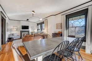 Een ruime woonkamer met een grote eettafel, zachte zithoeken, een open haard en grote ramen met uitzicht.