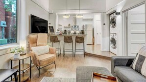 En modern lägenhet med kök, matplats och vardagsrum. Den innehåller en soffa, ett soffbord och en TV.