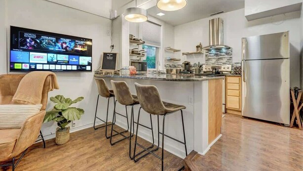 Ett modernt kök med en stor köksö, barstolar, ett kylskåp i rostfritt stål och en platt-TV som är monterad på väggen.