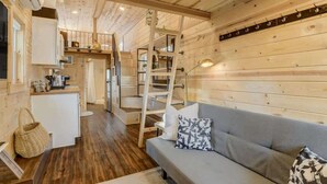 A wooden interior with a sofa, a ladder, a kitchen area, and a staircase.