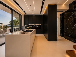 Une cuisine moderne dotée d’un îlot central, de meubles de rangement noirs et offrant une vue sur l’extérieur.