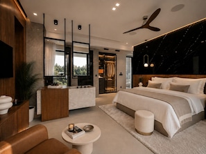 Un dormitorio moderno con una cama grande, tocador, rincón de descanso y vestidor.