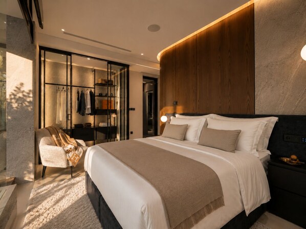 Une chambre moderne avec un grand lit, un coin salon avec un fauteuil et une armoire intégrée.
