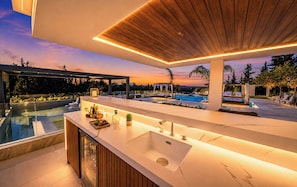 A modern kitchen with a large island, a pool, and a sunset view.