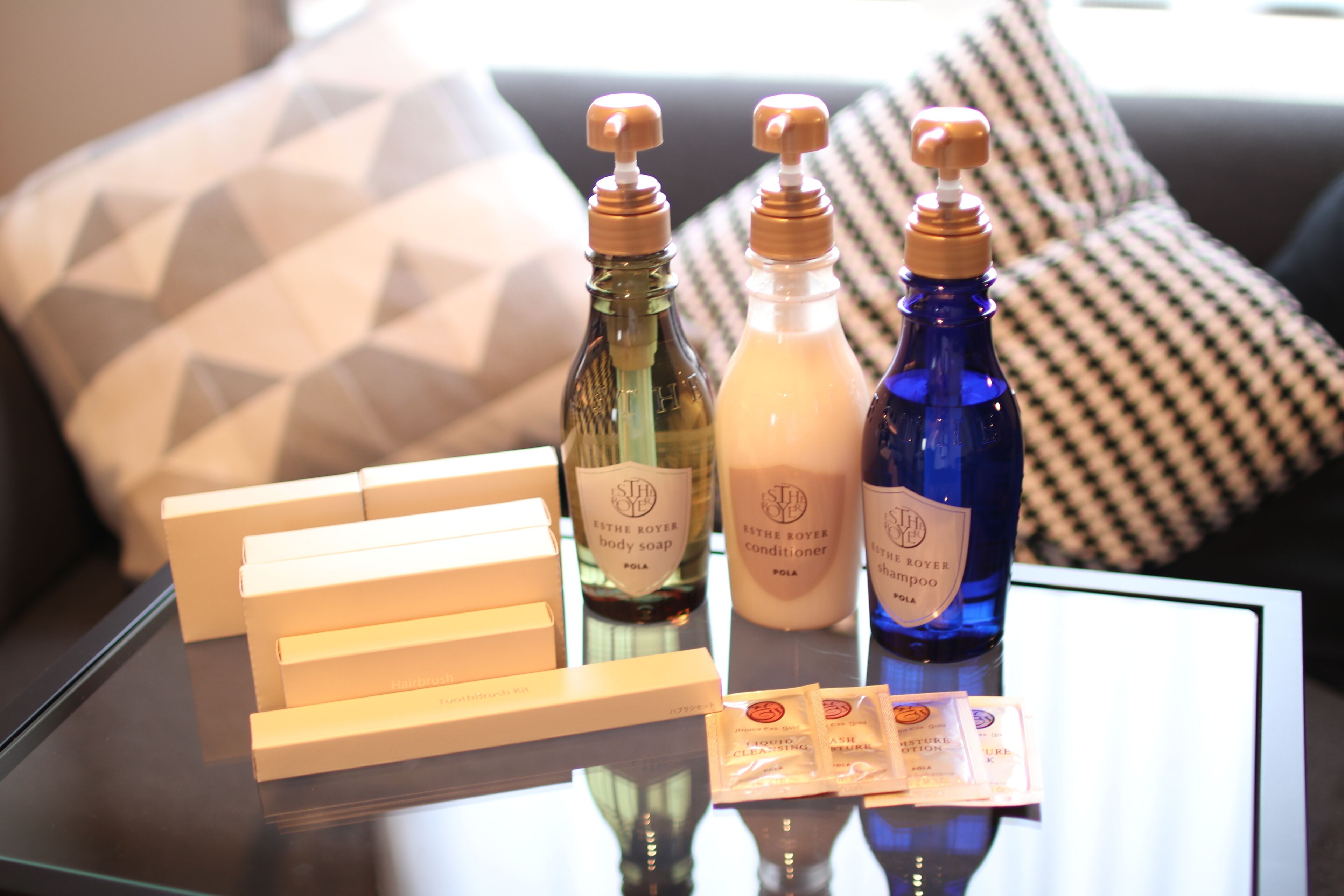 A table with bottles of body soap, conditioner, and shampoo, along with their packaging, on a glass surface.