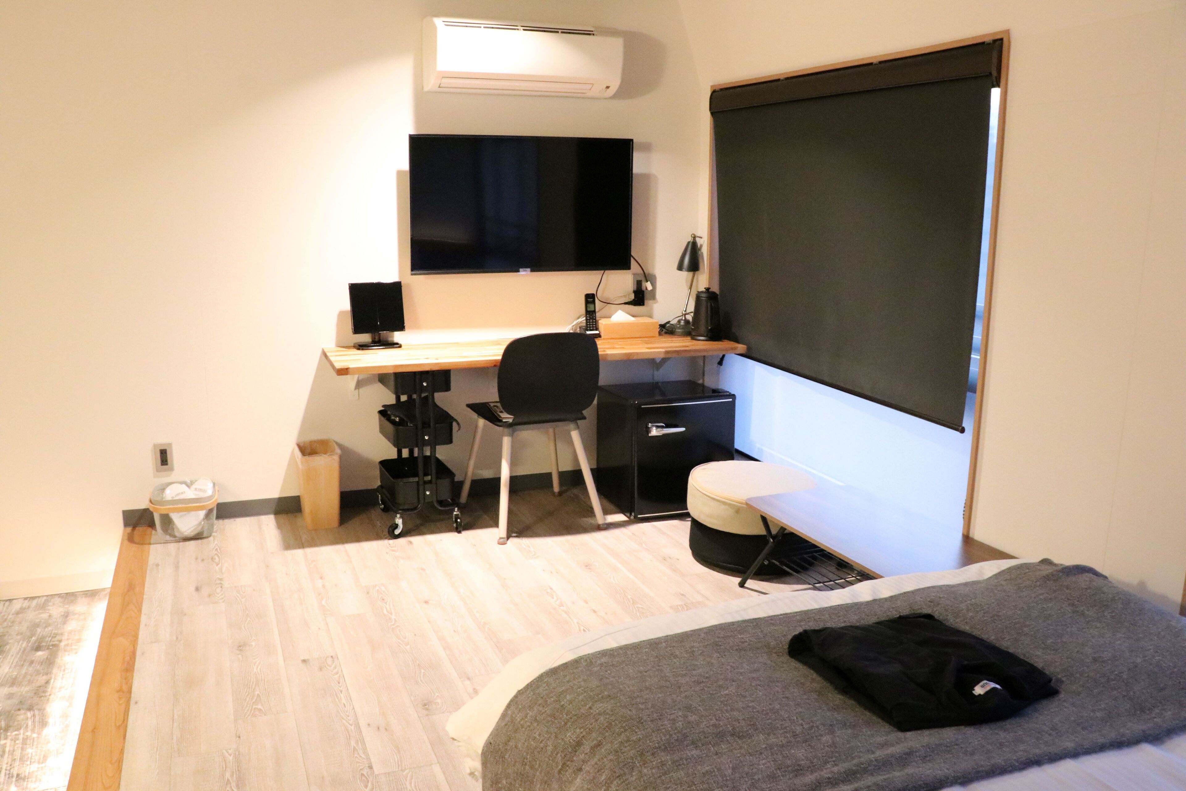 A bedroom with a bed, a desk, a chair, a TV, and a window.