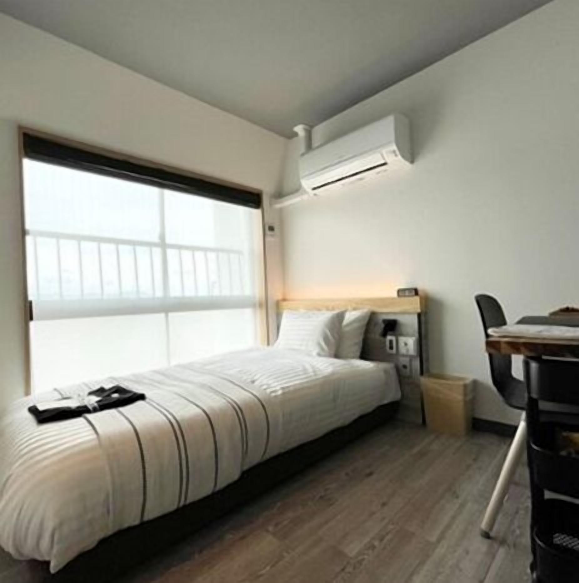 A small, modern bedroom with a bed, a desk, and a window.