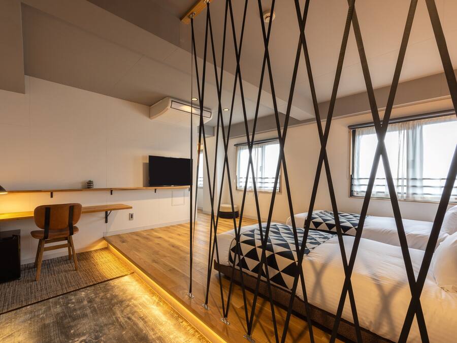 Una camera d'albergo moderna con pavimento in legno, un letto con testiera a motivi geometrici, una scrivania con sedia, una TV a schermo piatto e una finestra con tende.