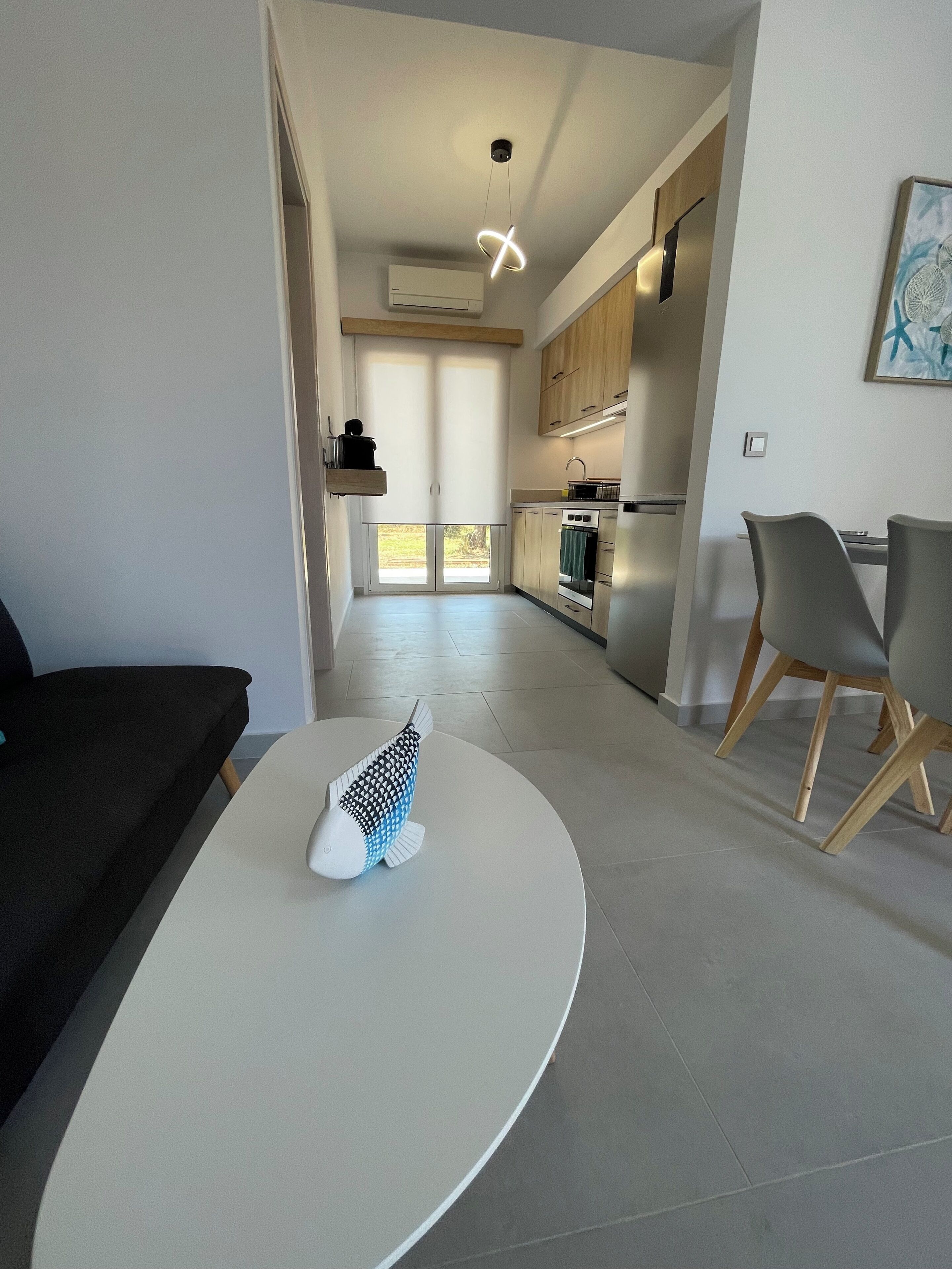 A modern kitchen with built-in appliances, a dining area with a table and chairs, and a view through a glass door.