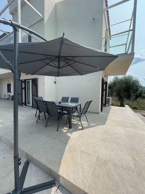Una terrazza all'aperto con tavolo e sedie, un ombrellone grande e un edificio moderno sullo sfondo.