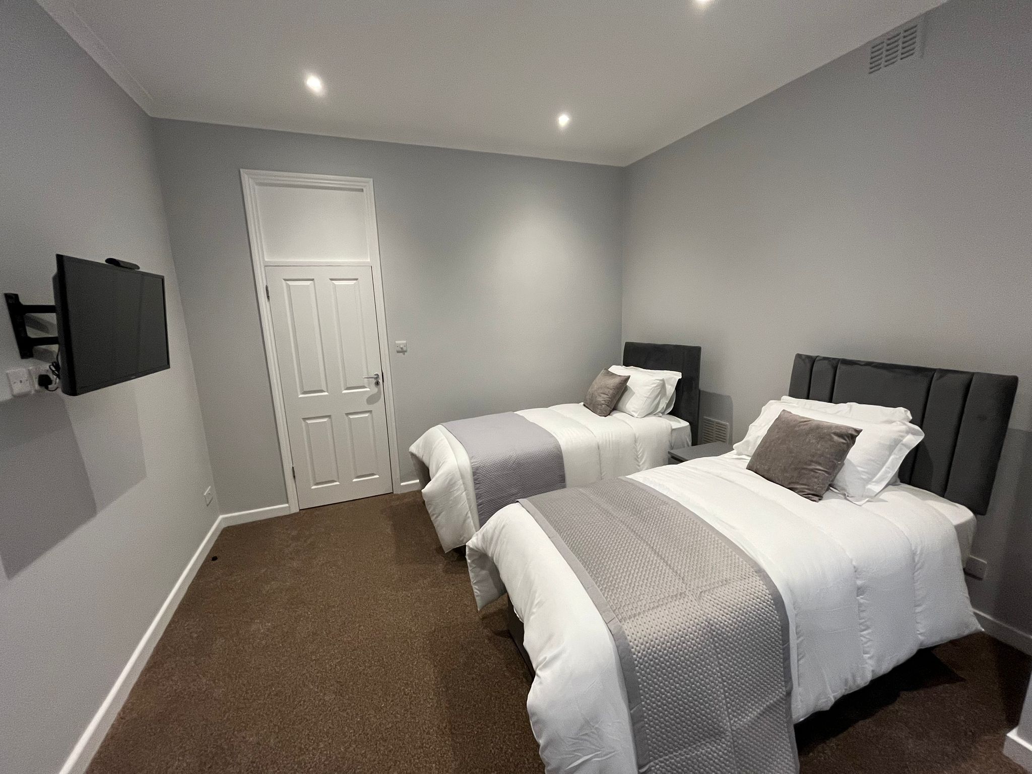 A bedroom with two beds, a door, and a mounted TV.