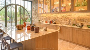 A modern kitchen with a large island, stone wall backsplash, and a view of greenery outside. - La Glycine (Tonnac)