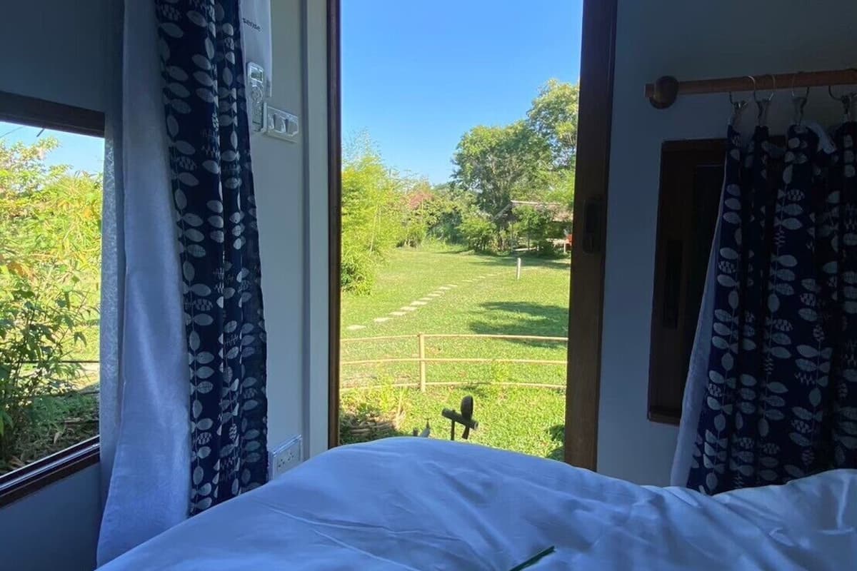 Een slaapkamer met een bed, een raam met gordijnen en uitzicht op een groen landschap.