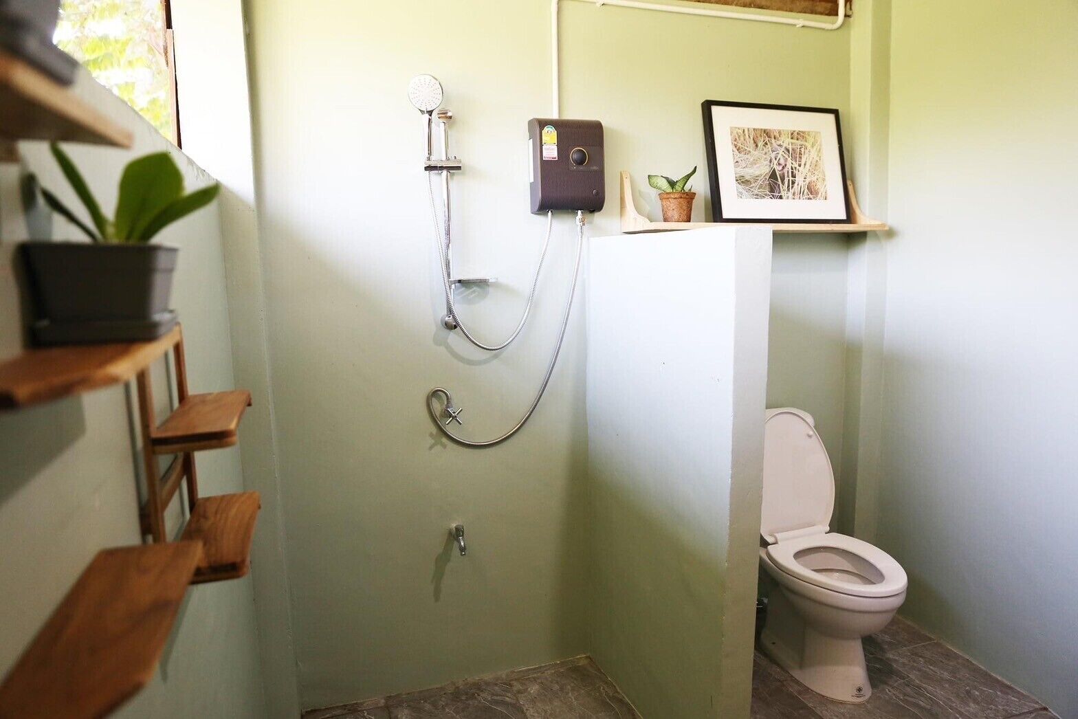 A small bathroom with a shower, toilet, and a shelf with a plant.