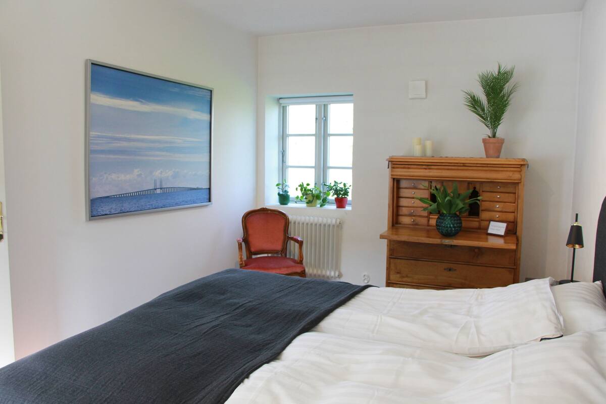 A bedroom with a bed, a chair, a dresser, a window, and a painting on the wall.