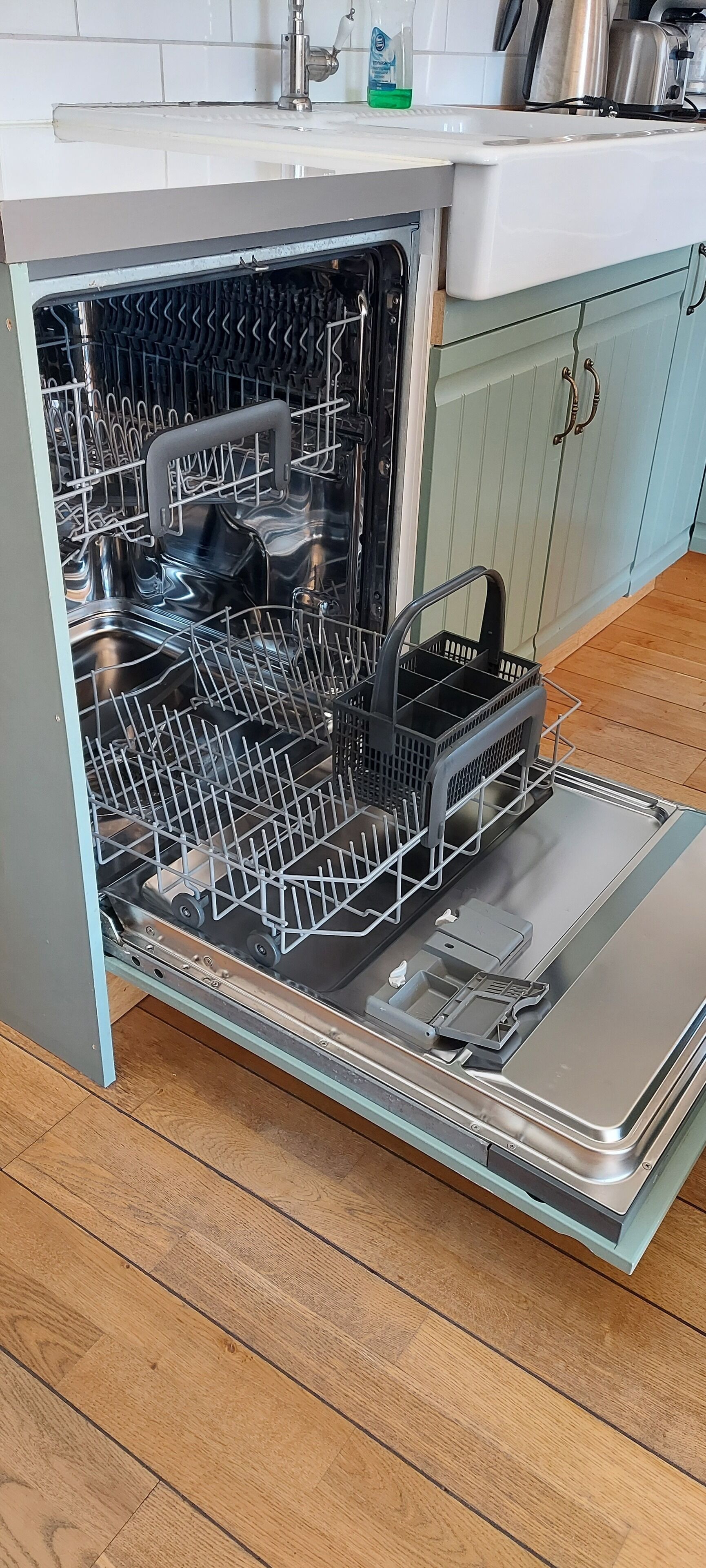 Een open vaatwasser in een keuken met een houten vloer en lichtblauwe kastjes.