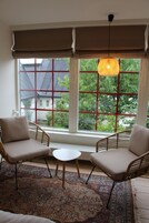 A room with two wicker chairs, a small round table, and a large window with red frames.