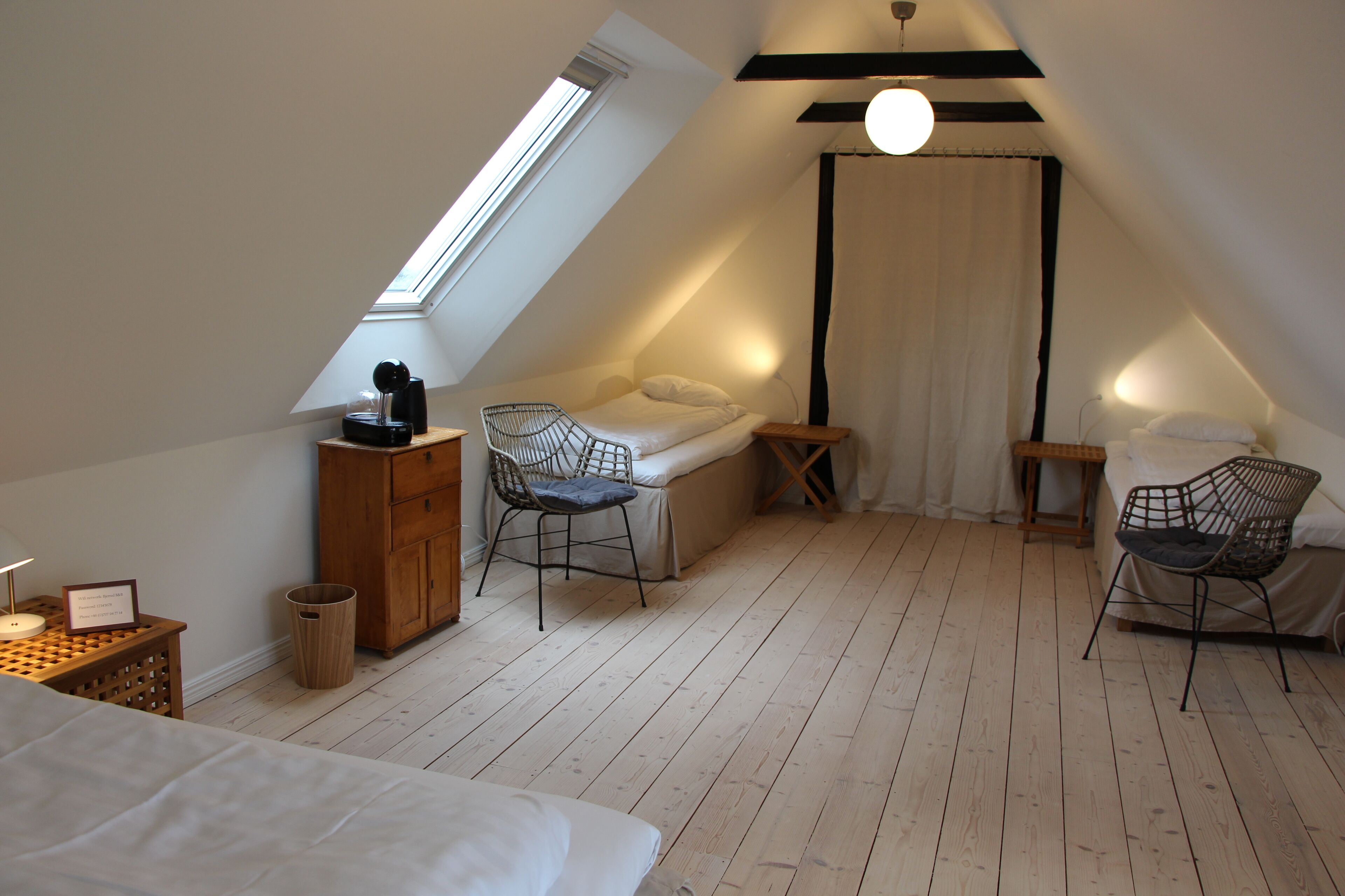 A cozy attic bedroom with a sloped ceiling, a skylight, a bed, two chairs, a small table, and a waste bin.