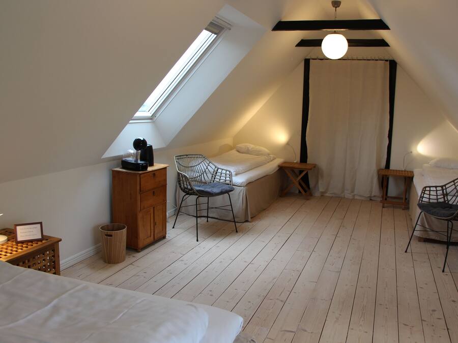 A cozy attic bedroom with a sloped ceiling, a skylight, a bed, two chairs, a small table, and a waste bin.