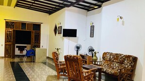 A spacious living area with a wooden ceiling, a sofa, a dining table with chairs, and a TV mounted on the wall. - Happy Resort Yala (Thissamaharama)