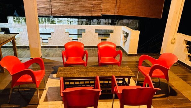 A dining area with a wooden table and six red chairs, a tiled floor, and a view of a building in the background. - Happy Resort Yala (Thissamaharama)