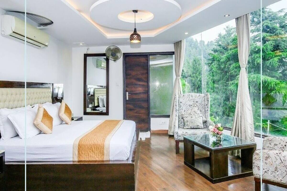 A modern bedroom with a large bed, a sitting area with a coffee table, and a view of greenery outside.