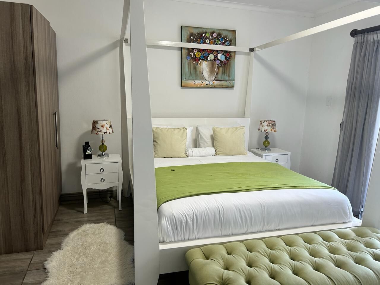Un dormitorio con cama de dos plazas, ropa de cama blanca, dos mesitas de noche con lámparas, una alfombra mullida y un cuadro sobre la cama.