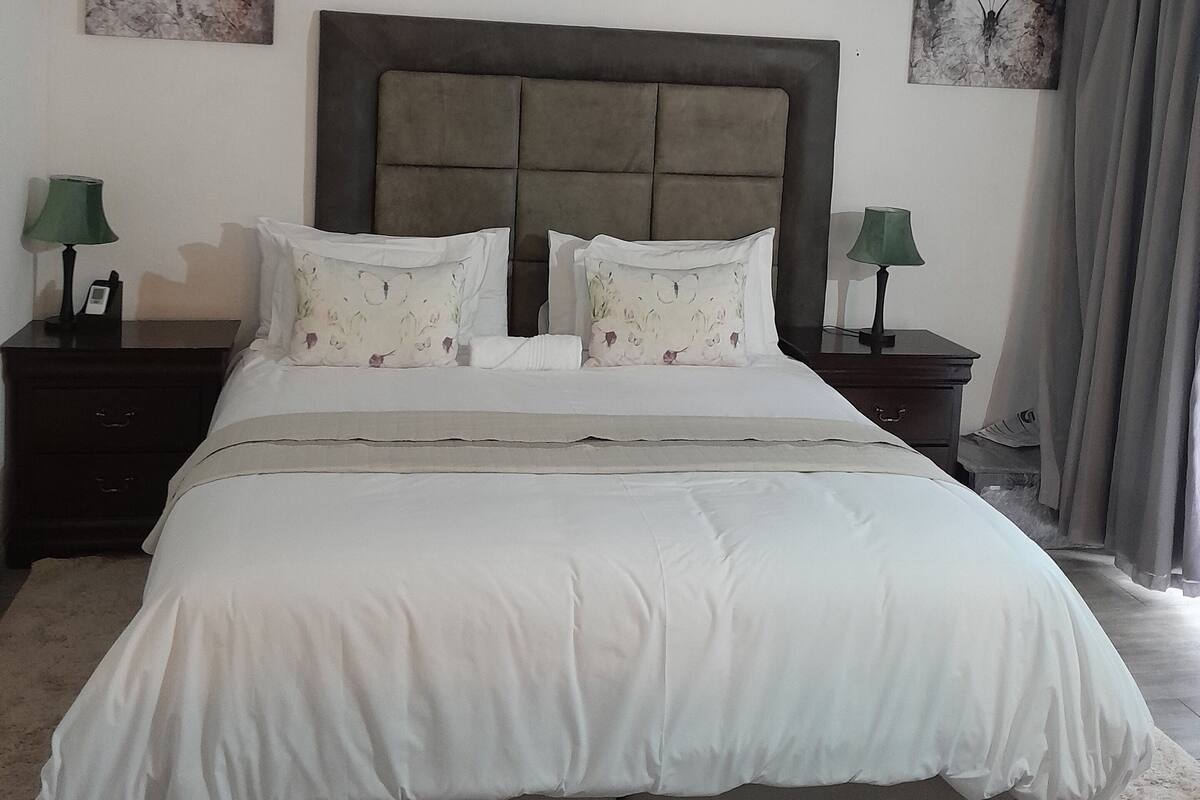 Een slaapkamer met een groot bed, twee nachtkastjes, een hoofdbord en twee wanddecoraties van vlinders.