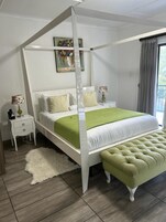 Una cama con dosel con un edredón verde, almohadas blancas y un banco verde a juego.