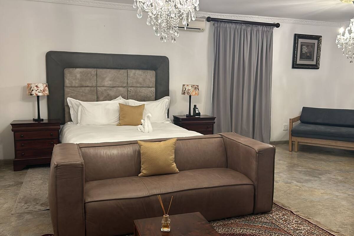Een slaapkamer met een groot bed, een bruine bank, een houten bankje en twee nachtkastjes met lampen.