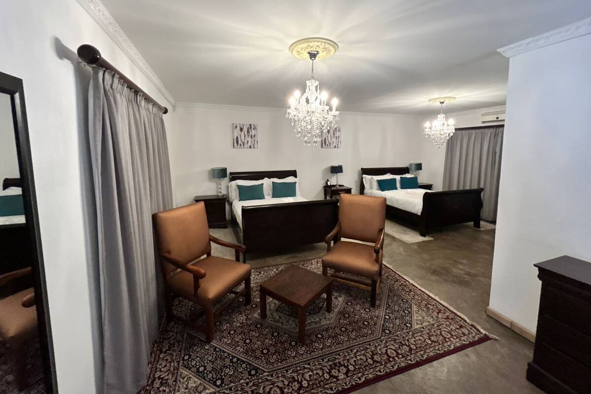 Een hotelkamer met twee bedden, een kroonluchter, een grote spiegel en een kamerkleed met dessin.